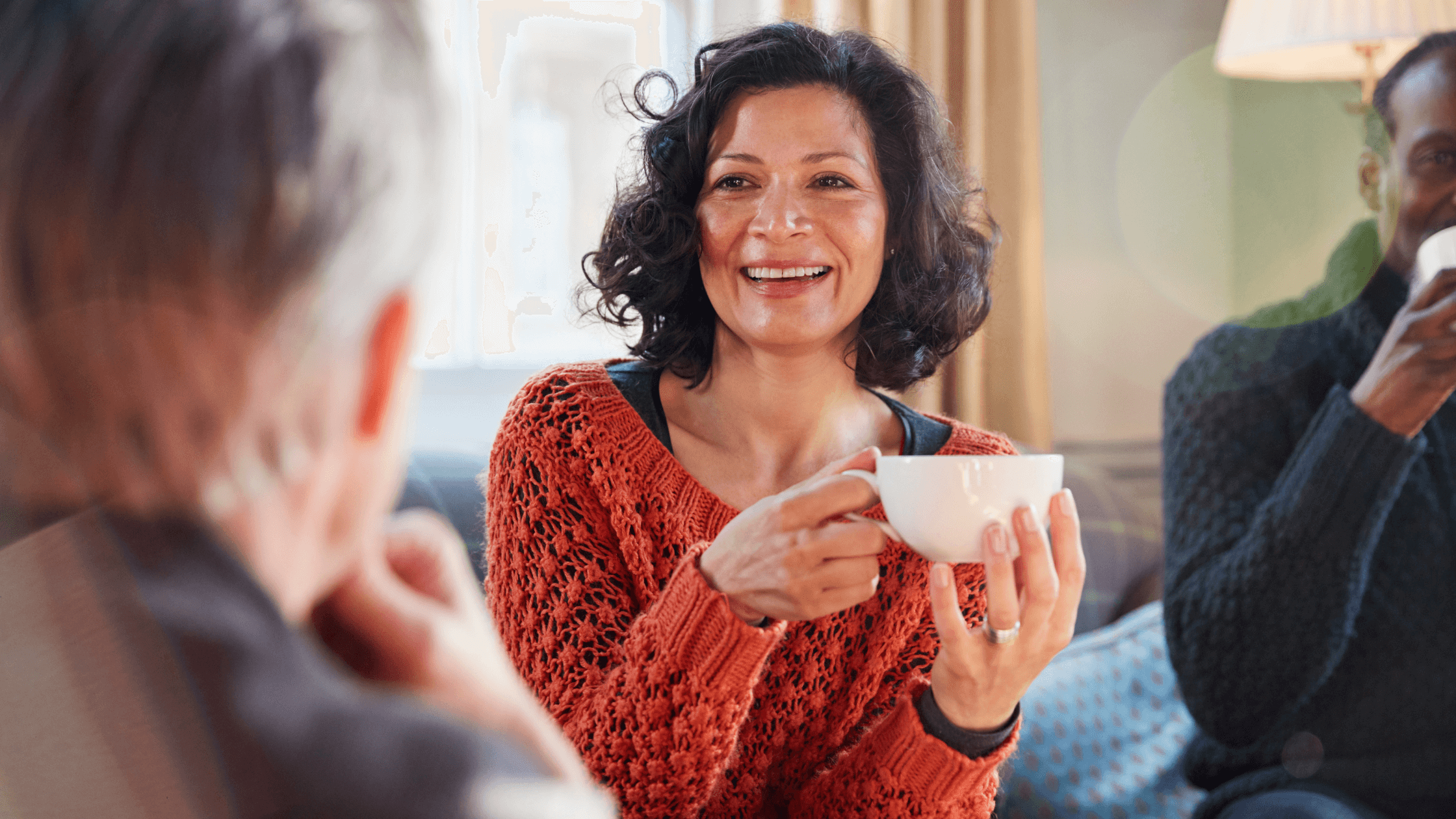 A smiling postmenopausal woman in her 50s, holding a cup of coffee and engaging in conversation, representing restored confidence and wellness achieved through a combination of hormone replacement therapy and GLP-1 medical weight loss programs in Colleyville, Fort Worth, or Southlake.